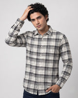 A man wearing a long-sleeve plaid button-up shirt in black, white, and gray, posed against a light gray studio background.