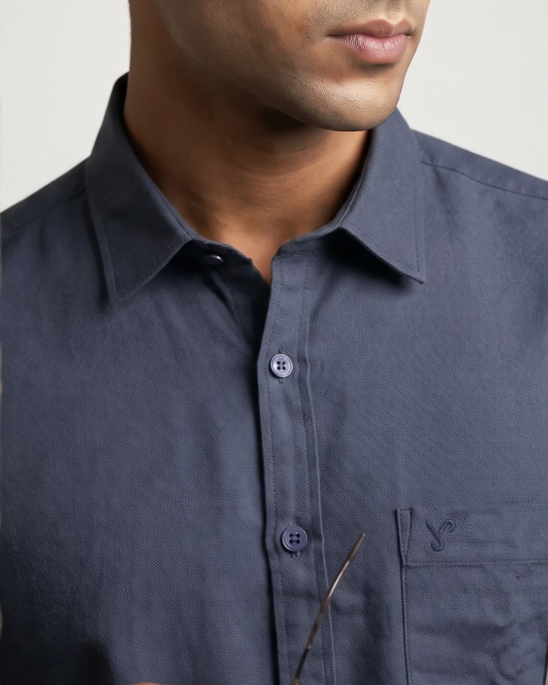 Close-up of a man wearing a dark slate blue button-down shirt with a chest pocket and a small embroidered logo.