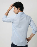 A man wearing a light blue long-sleeve linen shirt, shown from the back against a plain light gray studio background.