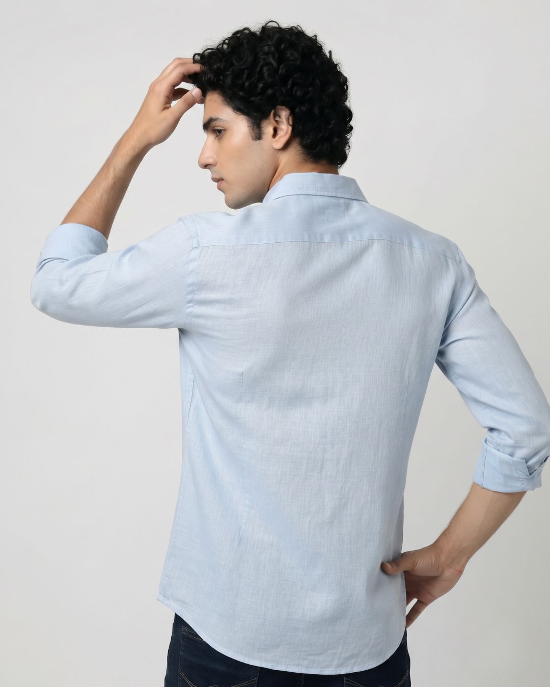 A man wearing a light blue long-sleeve linen shirt, shown from the back against a plain light gray studio background.