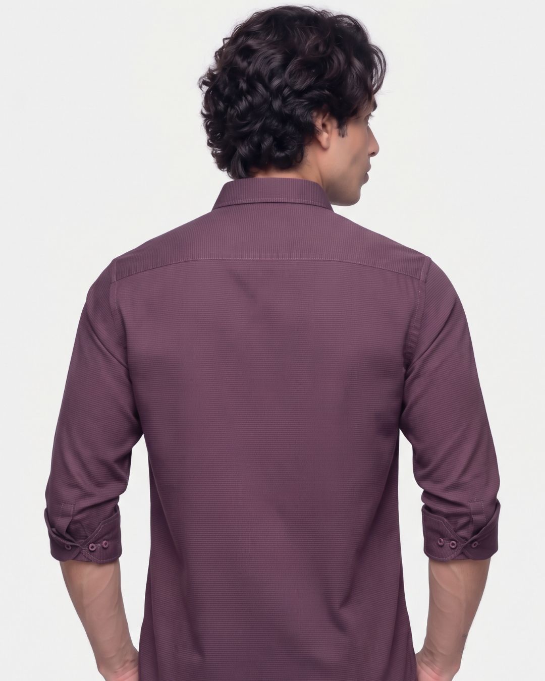 A man viewed from the back wearing a long-sleeve button-up shirt in a muted plum or mauve-purple color, set against a plain light gray studio background.