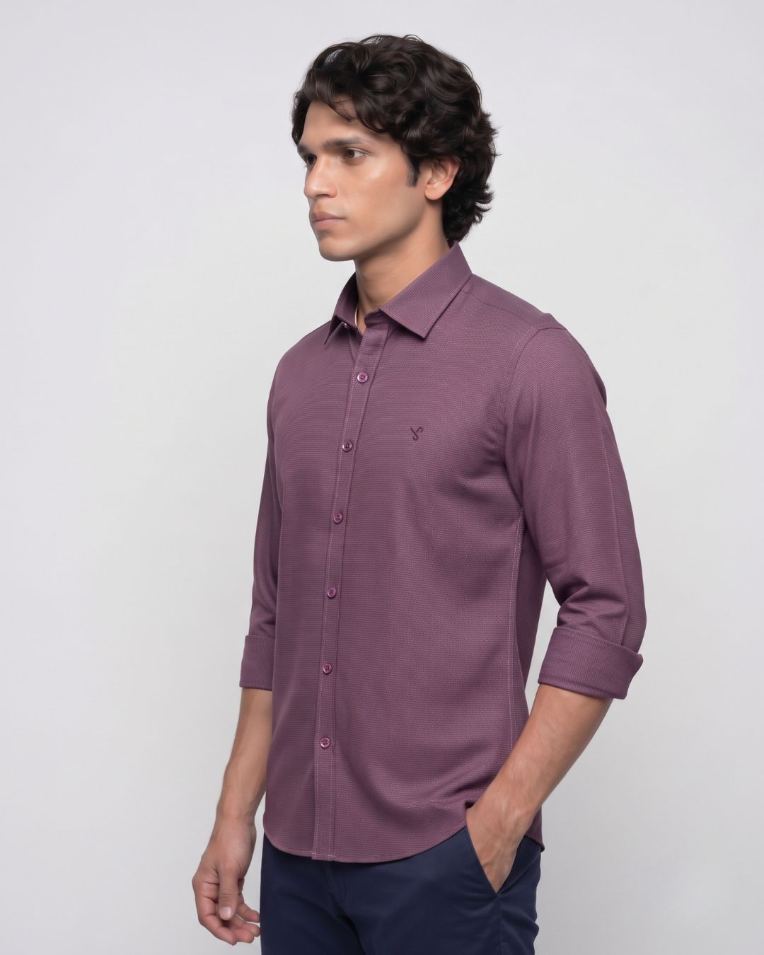 A man wearing a long-sleeve button-down shirt in a dusty purple shade, paired with navy trousers, standing against a light gray studio background.