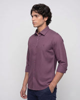 A man wearing a long-sleeve button-down shirt in a dusty purple shade, paired with navy trousers, standing against a light gray studio background.