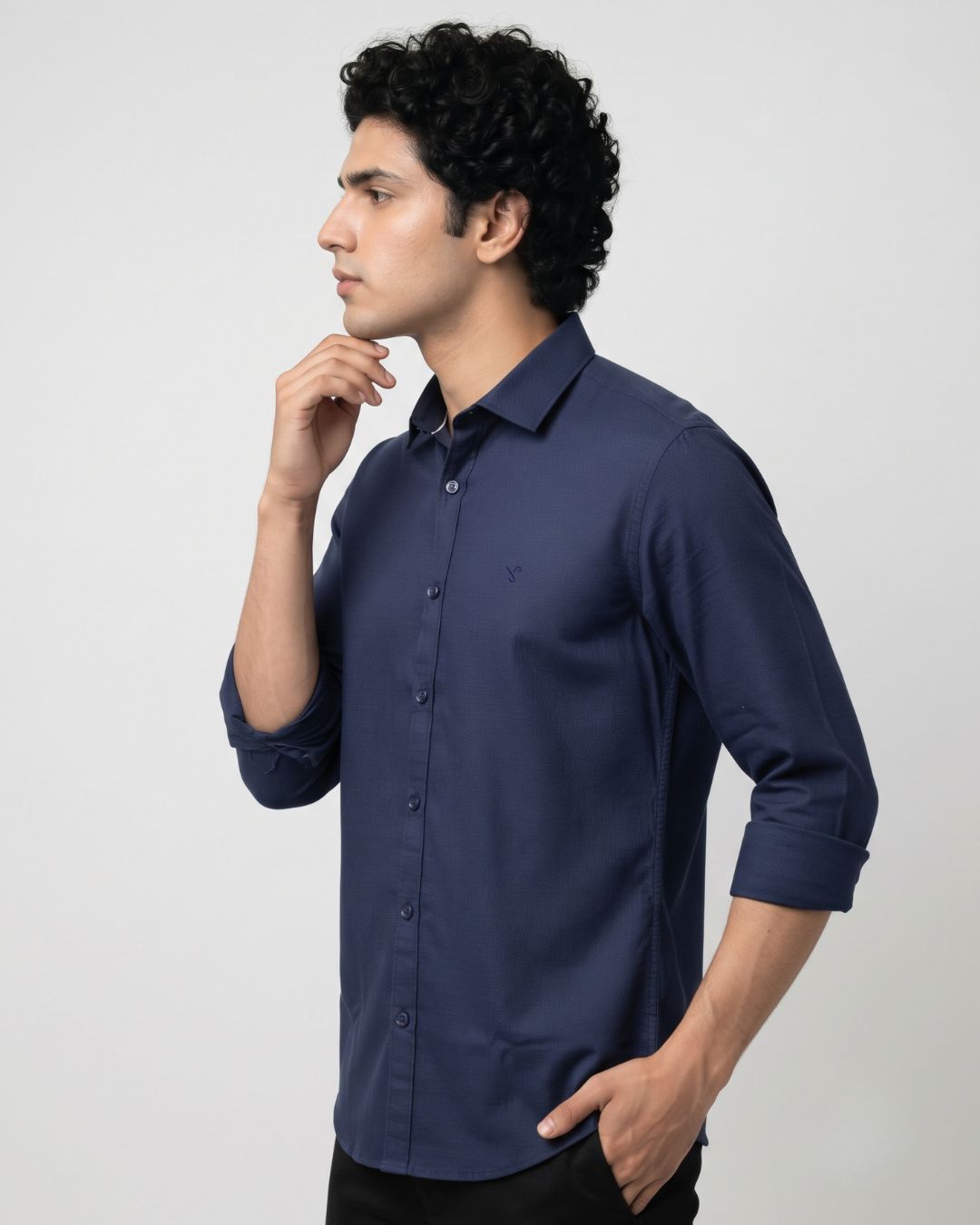 A man wearing a navy blue long-sleeve button-down shirt, shown in a side profile against a light gray studio background.
