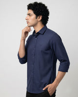 A man wearing a navy blue long-sleeve button-down shirt, shown in a side profile against a light gray studio background.