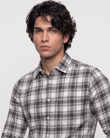 A man wearing a gray and white plaid button-down shirt, photographed from the chest up against a light gray studio background.