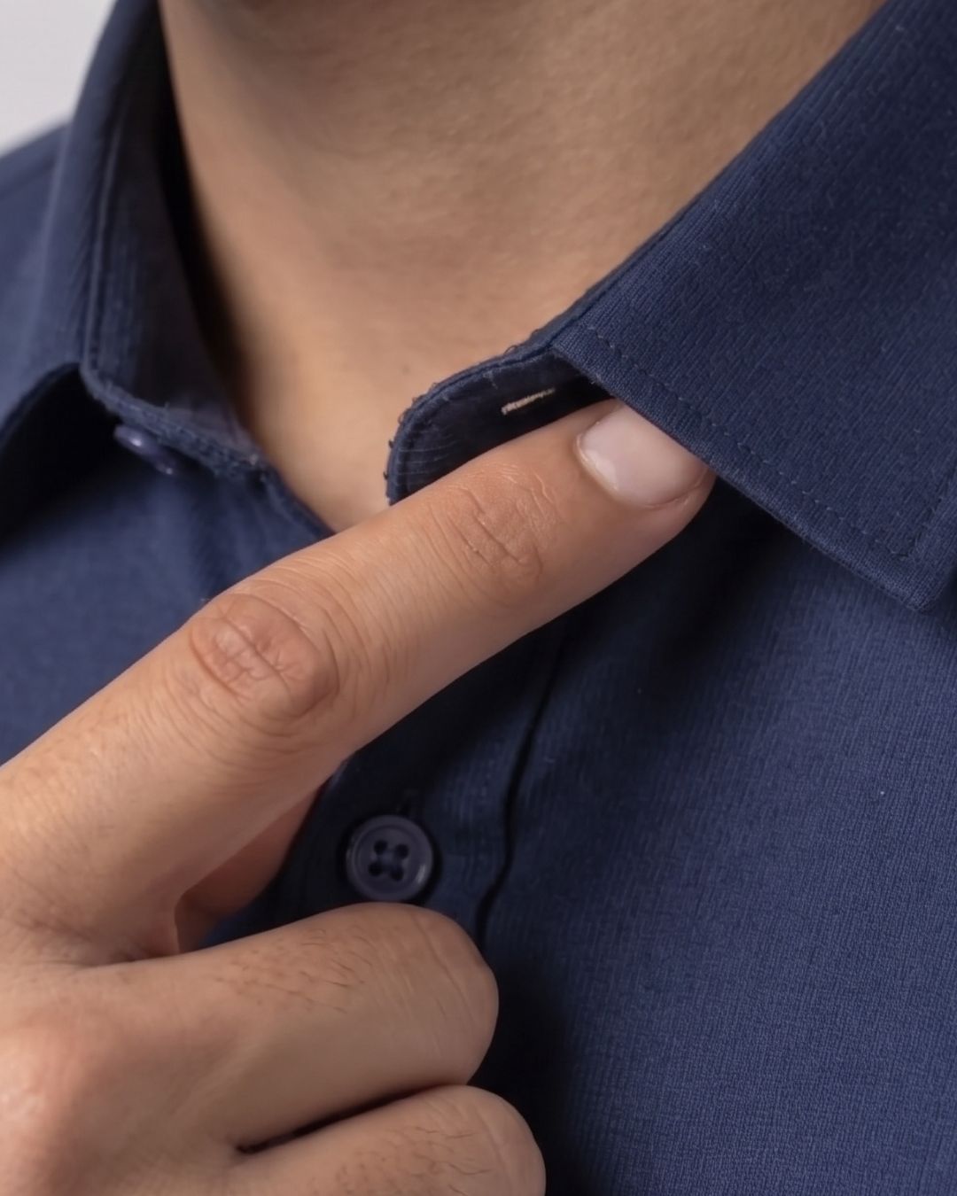 Close-up of a person wearing a dark navy blue button-down shirt, with their finger pointing to the collar area.