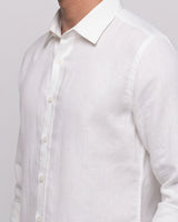 A close-up of a white long-sleeve linen button-down shirt worn by a model, showing the collar, front buttons, and textured fabric against a light gray background.