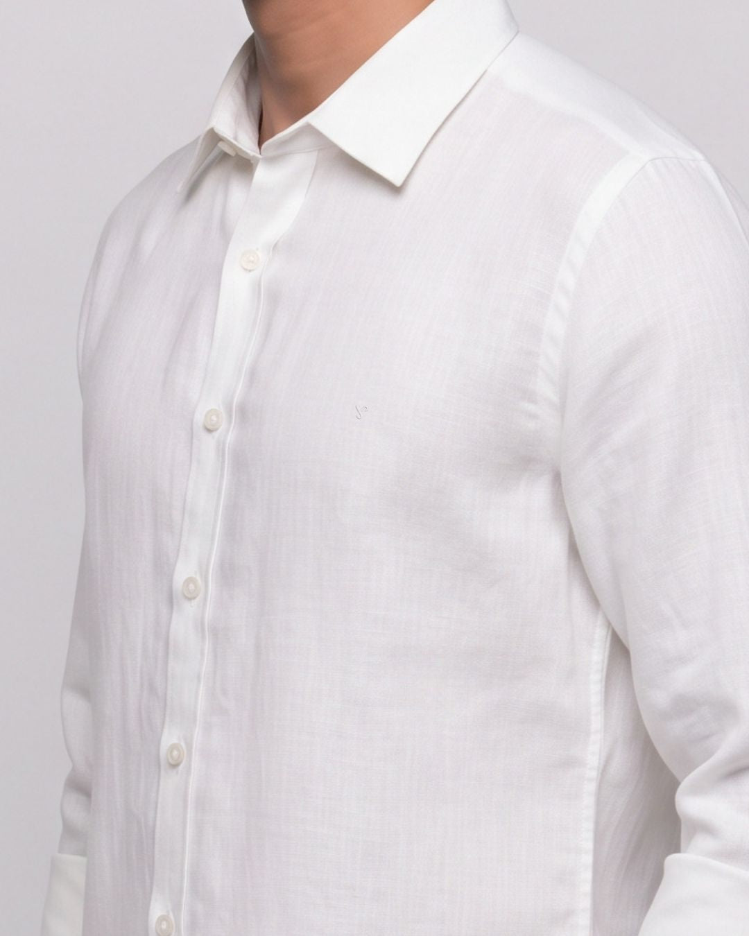 A close-up of a white long-sleeve linen button-down shirt worn by a model, showing the collar, front buttons, and textured fabric against a light gray background.