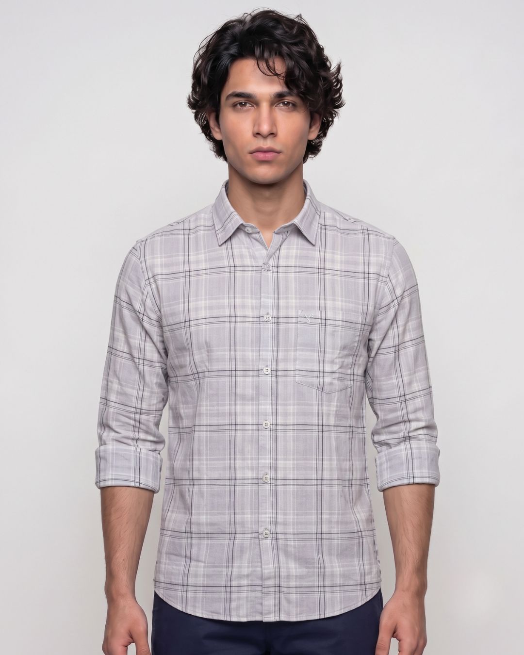 A man wearing a light gray and white plaid long-sleeve button-down shirt, shown from the waist up against a plain light gray studio background.