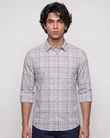 A man wearing a light gray and white plaid long-sleeve button-down shirt, shown from the waist up against a plain light gray studio background.
