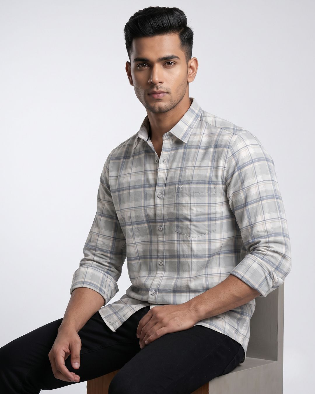 A man wearing a light gray and white plaid button-down shirt, posing with his back turned and leaning against a textured concrete pillar.