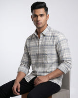 A man wearing a light gray and white plaid button-down shirt, posing with his back turned and leaning against a textured concrete pillar.