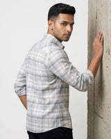A man wearing a light gray and white plaid button-down shirt, posing with his back turned and leaning against a textured concrete pillar.