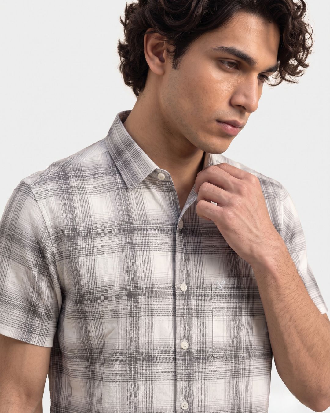A man wearing a short-sleeve plaid button-up shirt in light gray and white, shown from the chest up against a plain light gray background.