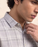 A close-up of a man wearing a light gray and white plaid button-down shirt, adjusting the collar with one hand.