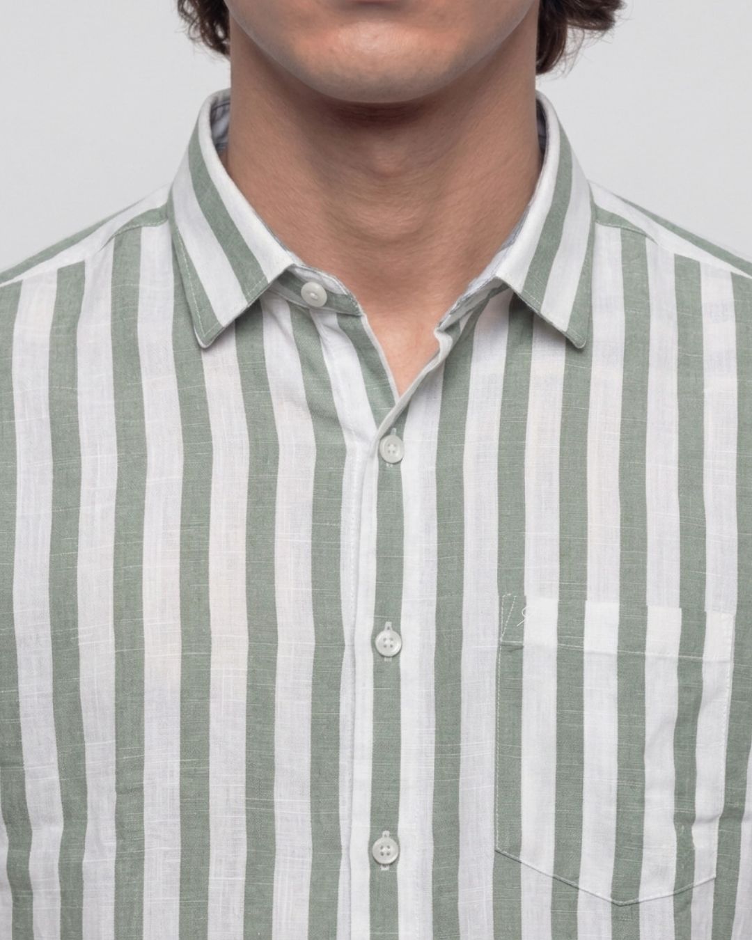 A close-up of a man wearing a light green and white vertically striped linen button-down shirt.