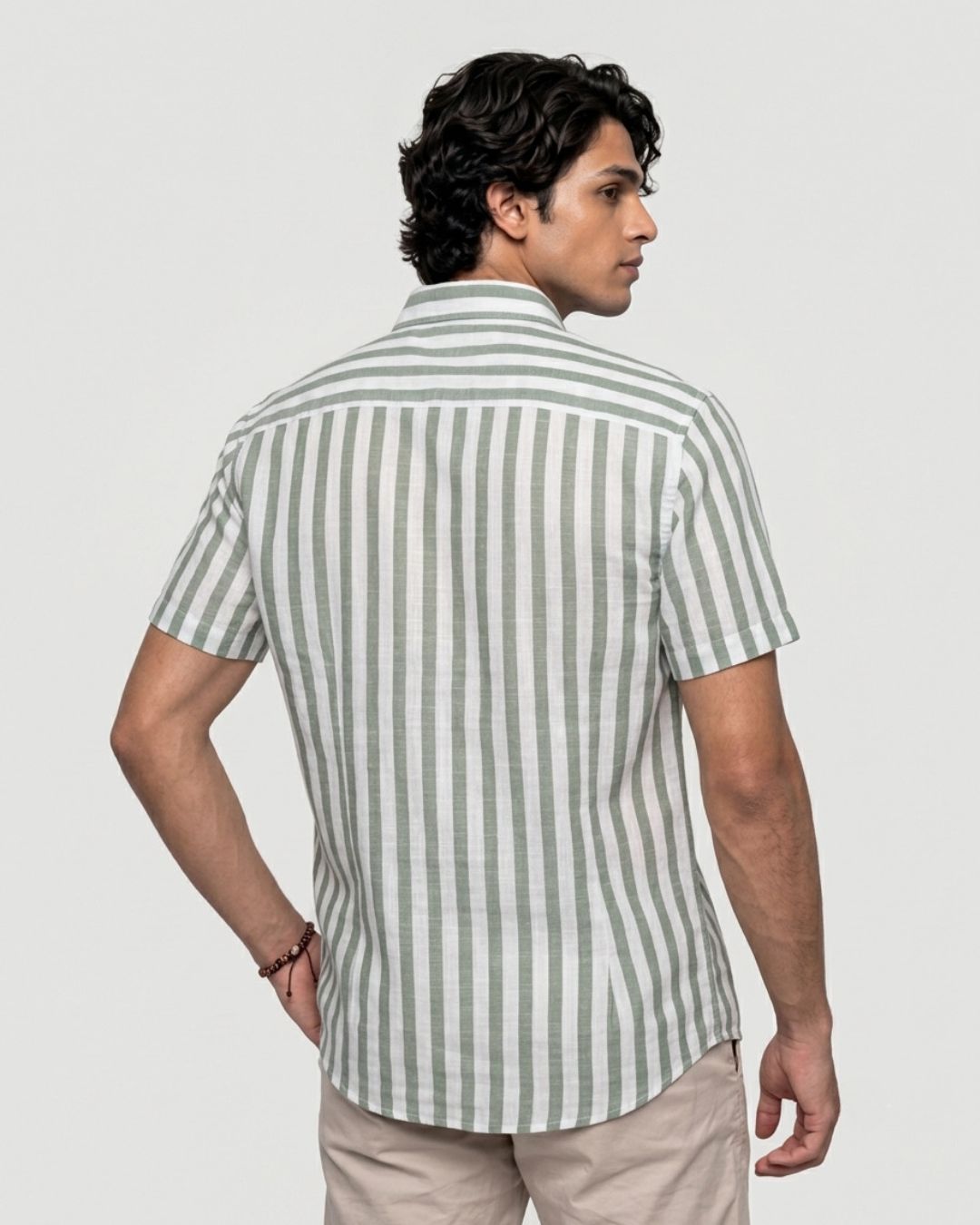 A man wearing a short-sleeve button-up shirt with vertical sage green and white stripes, shown from the back against a light gray studio background.