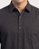 A close-up of a man wearing a dark charcoal gray button-down shirt with a subtle geometric jacquard pattern and a chest pocket.