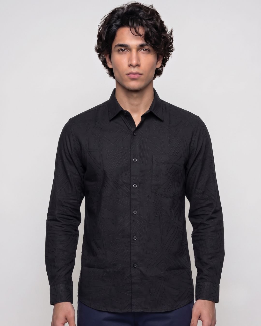 A man wearing a black long-sleeve button-up shirt with a subtle tonal jacquard pattern, photographed against a light gray studio background.