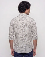 A man viewed from the back wearing a light beige long-sleeve button-up shirt with a gray floral pattern, paired with navy blue pants, against a plain white background.