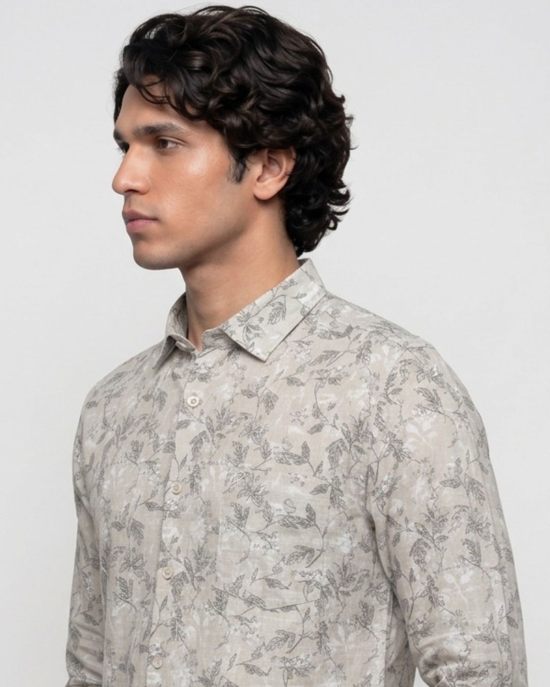 A man wearing a light beige long-sleeve button-up shirt with a gray botanical leaf pattern, shown in a side-profile view against a plain light gray background.