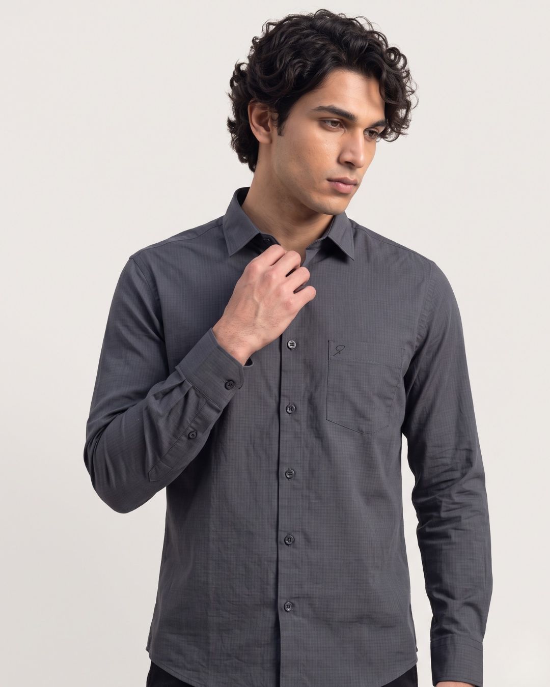 A man wearing a dark gray long-sleeve button-down shirt, posing against a light gray studio background.