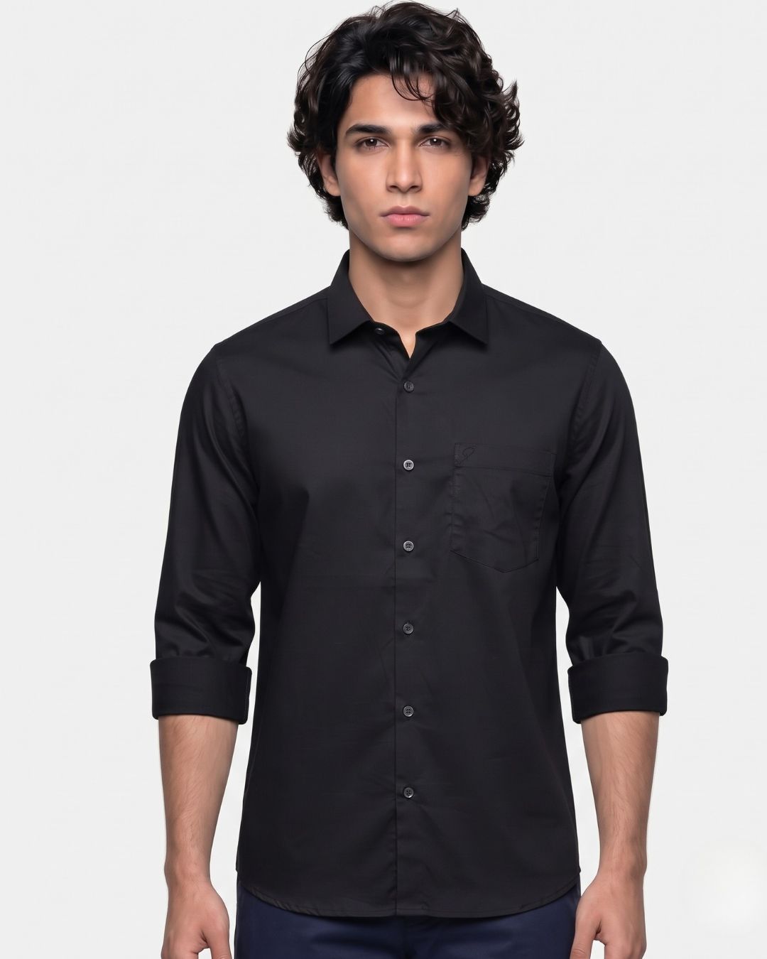 A man wearing a black long-sleeve button-down shirt with rolled-up cuffs, shown against a plain light gray studio background.