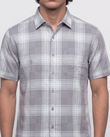 A man wearing a short-sleeve button-up plaid shirt in gray and white, shown from the neck down against a light gray background.