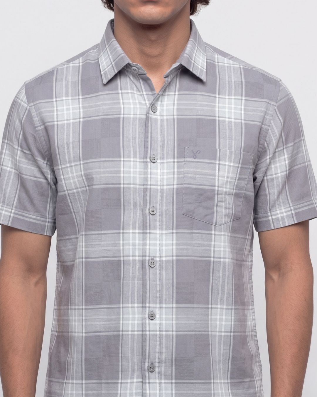 A man wearing a short-sleeve button-up plaid shirt in gray and white, shown from the neck down against a light gray background.