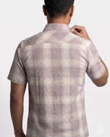 A man viewed from the back wearing a short-sleeve plaid button-up shirt in muted taupe and cream, against a plain light gray studio background.