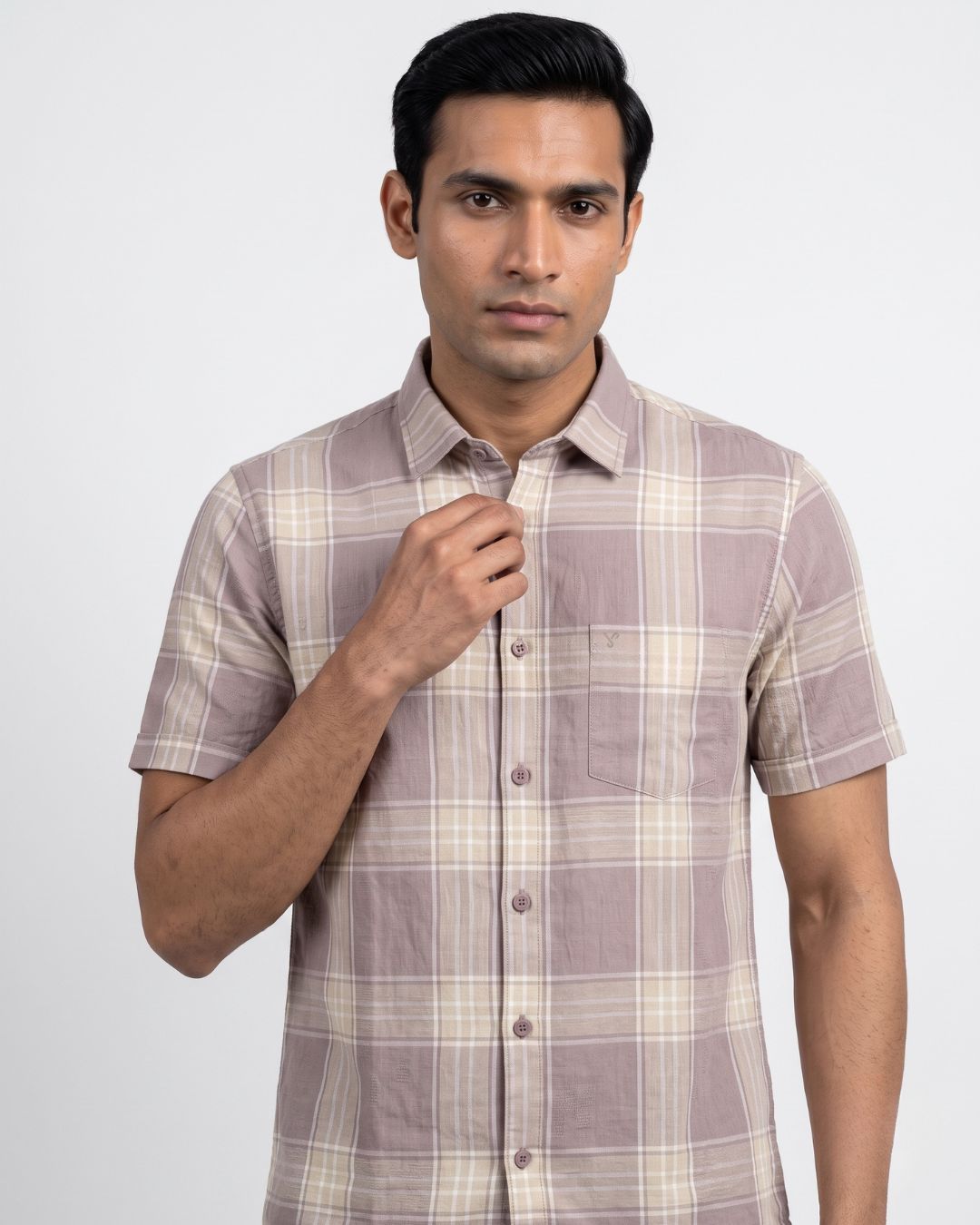 A man wearing a short-sleeve button-up shirt with a beige and taupe plaid pattern, standing against a light gray studio background.