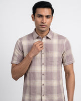 A man wearing a short-sleeve button-up shirt with a beige and taupe plaid pattern, standing against a light gray studio background.