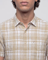 A close-up of a man wearing a short-sleeve button-up shirt with a beige and white plaid pattern. The shirt features a classic collar, button-down front, and a small embroidered logo on the left chest pocket.