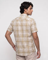 A man wearing a beige and white plaid short-sleeve button-up shirt, shown from a three-quarter back view against a plain light gray studio background.