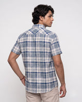 A man wearing a short-sleeve plaid button-up shirt in blue, white, and gray, shown from a three-quarters back view against a light gray studio background.