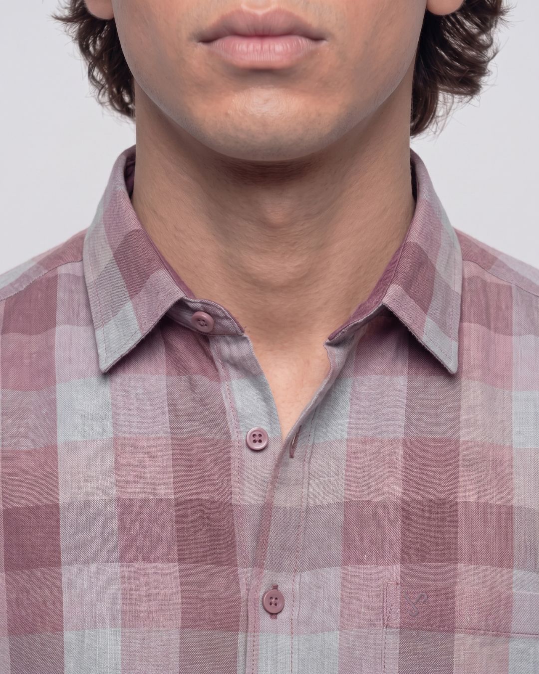 Close-up of a man wearing a pink and gray plaid button-down shirt, showing the collar, buttons, and chest pocket area.