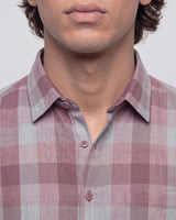 Close-up of a man wearing a pink and gray plaid button-down shirt, showing the collar, buttons, and chest pocket area.