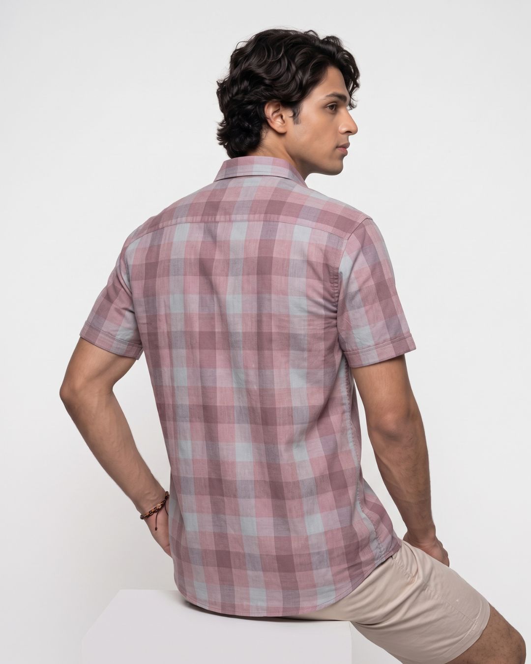 A man wearing a short-sleeve plaid button-up shirt in dusty pink and light blue, shown from the back and side against a plain white studio background.