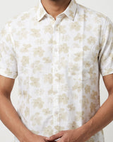 A man wearing a short-sleeve button-up shirt with a beige floral pattern on a white background, cropped from the neck to the waist.