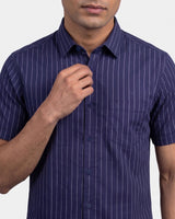 A man wearing a short-sleeve button-up shirt in navy blue with thin white vertical pinstripes, shown from the chin down against a light gray background.