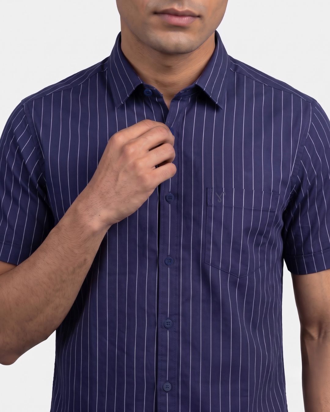 A man wearing a short-sleeve button-up shirt in navy blue with thin white vertical pinstripes, shown from the chin down against a light gray background.