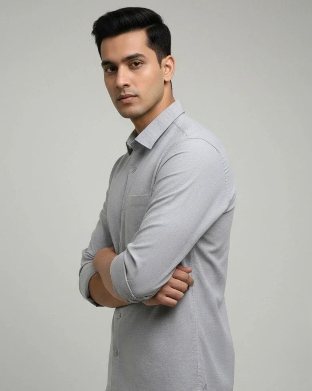 A man wearing a light gray long-sleeve button-up shirt, standing with arms crossed against a plain light gray studio background.