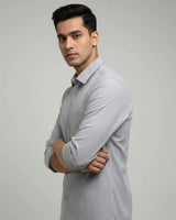 A man wearing a light gray long-sleeve button-up shirt, standing with arms crossed against a plain light gray studio background.