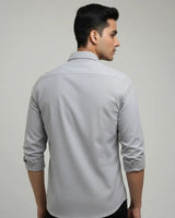 A man wearing a light gray long-sleeve button-down shirt, shown from the back and side profile against a plain light gray studio background.