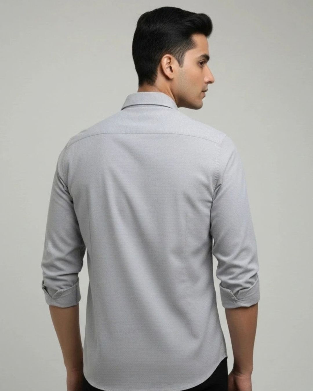 A man wearing a light gray long-sleeve button-down shirt, shown from the back and side profile against a plain light gray studio background.