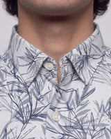 Close-up of a man wearing a white button-down shirt with a blue-gray palm leaf pattern, showing the collar, buttons, and neck area.