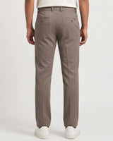 A person shown from the back wearing straight-leg trousers in a taupe-brown color, paired with white sneakers against a light gray studio background.
