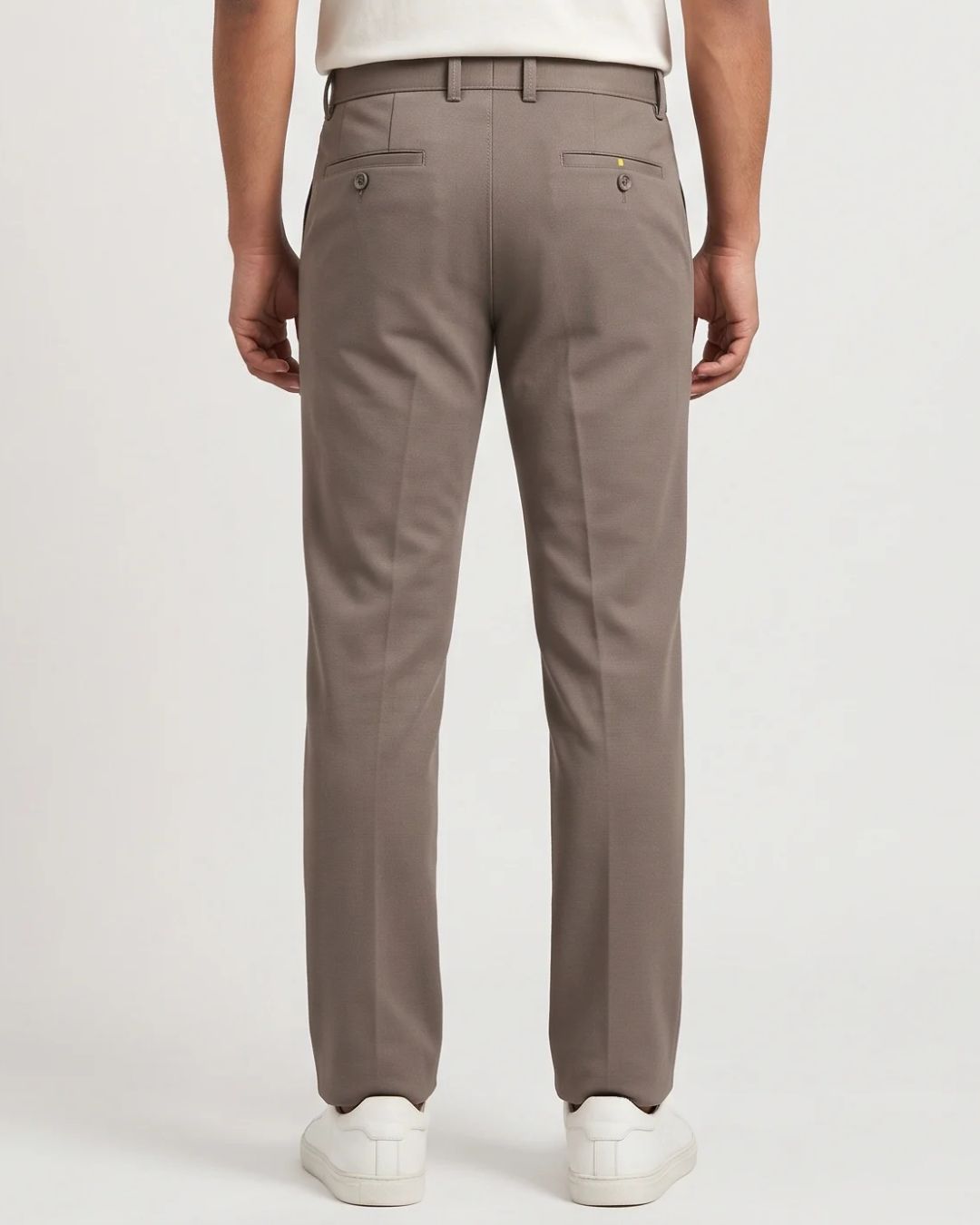A person shown from the back wearing straight-leg trousers in a taupe-brown color, paired with white sneakers against a light gray studio background.