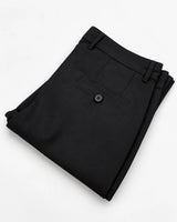 A pair of folded black dress pants with a buttoned welt pocket, shown on a clean white background.